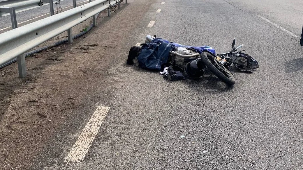 Повалений синій мотоцикл лежить на асфальті біля металевого відбійника